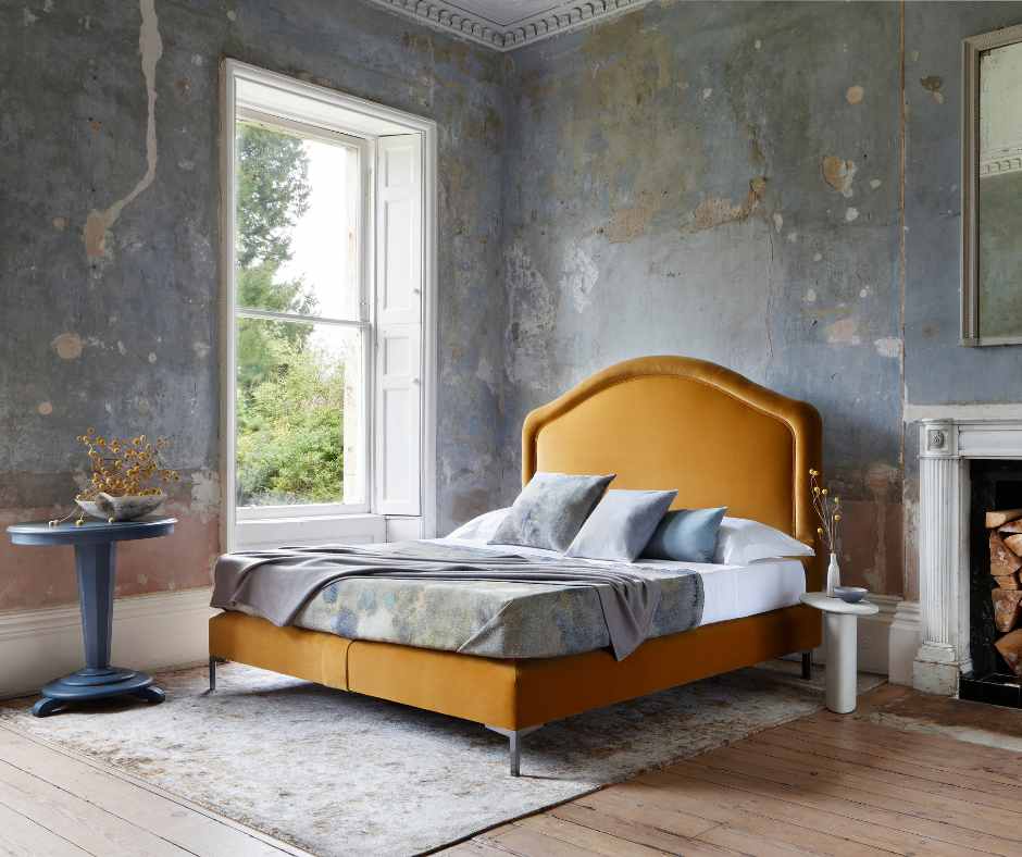 Savoir bed with a mustard headboard and soft edges and charming curves in a bedroom with large window