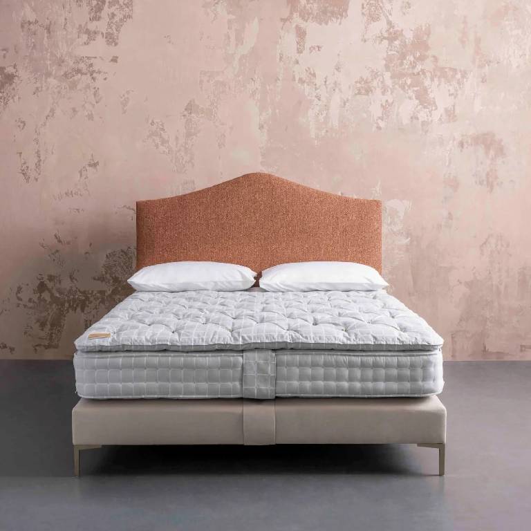 Handmade savoir no5 savvy mattress with headboard and topper set against a pale pink rustic background
