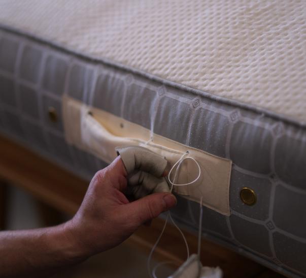 A Savoir beds craftsman is putting the final touches on the handle of a handcrafted mattress.